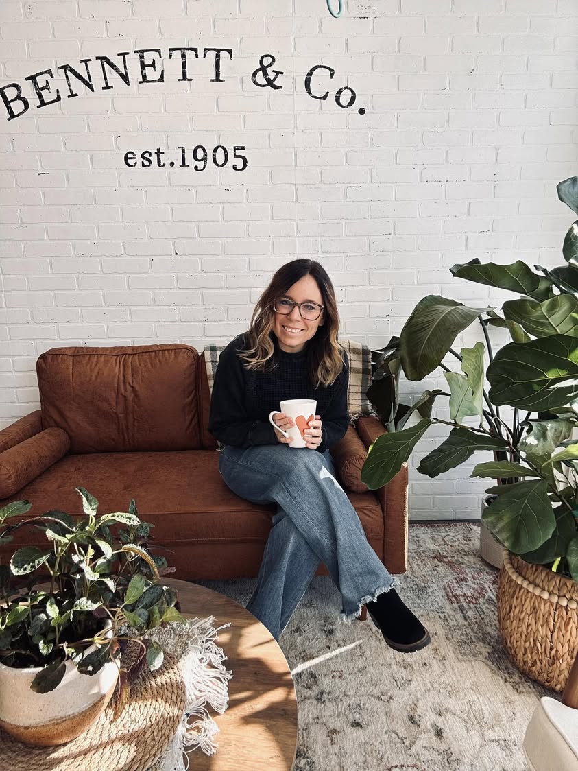Jenni sitting on a leather couch in the shop with a coffee mug